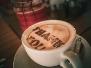White saucer and  Coffee mug with text "Thank You" on the foam. Background is reflective table.