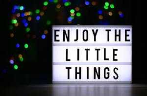 Glowing sign with "Enjoy the little things" text; green, blue, and brown lights in a black background